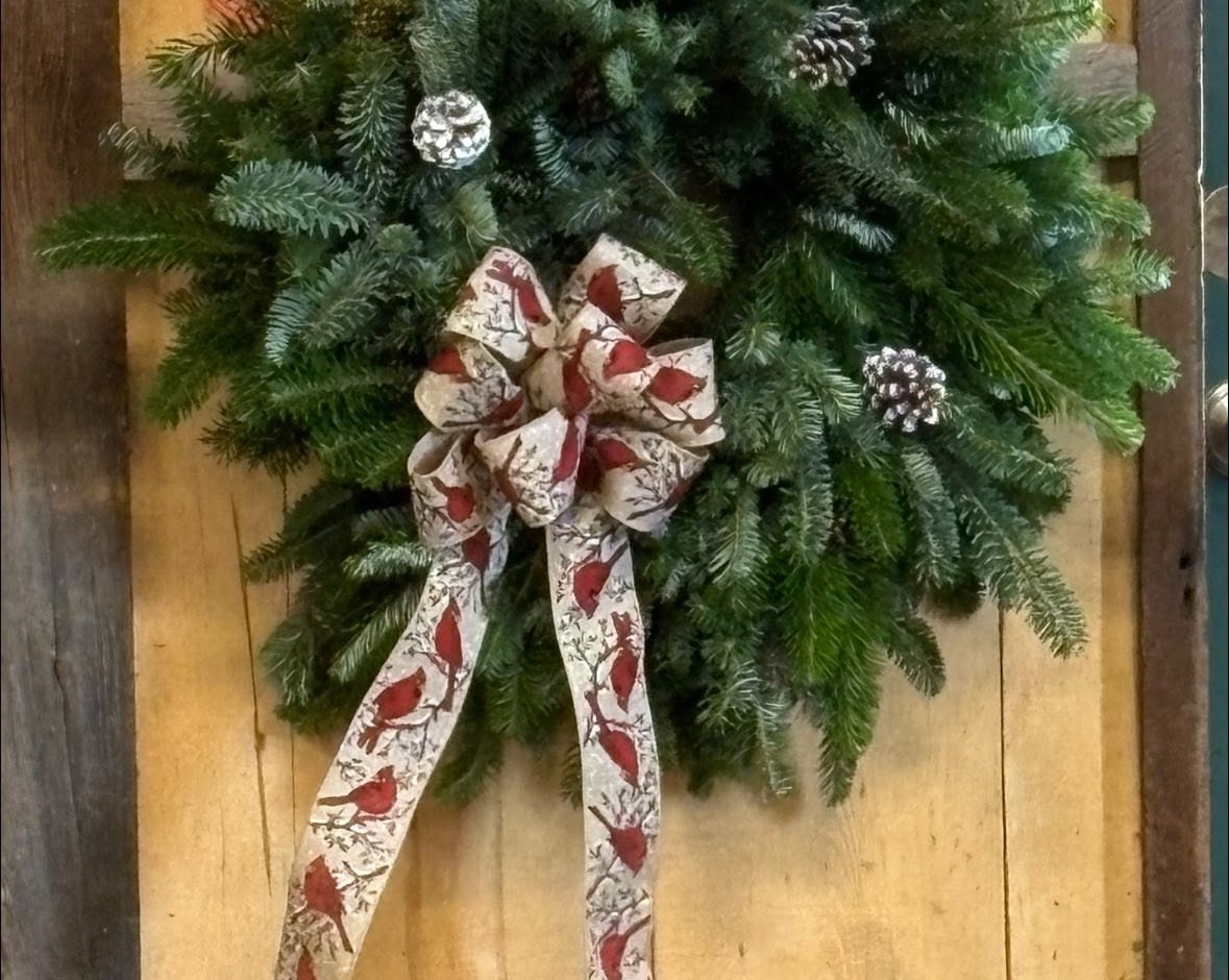 Fresh balsam wreath with pinecones and a cardinal-print ribbon bow hanging on barn wood