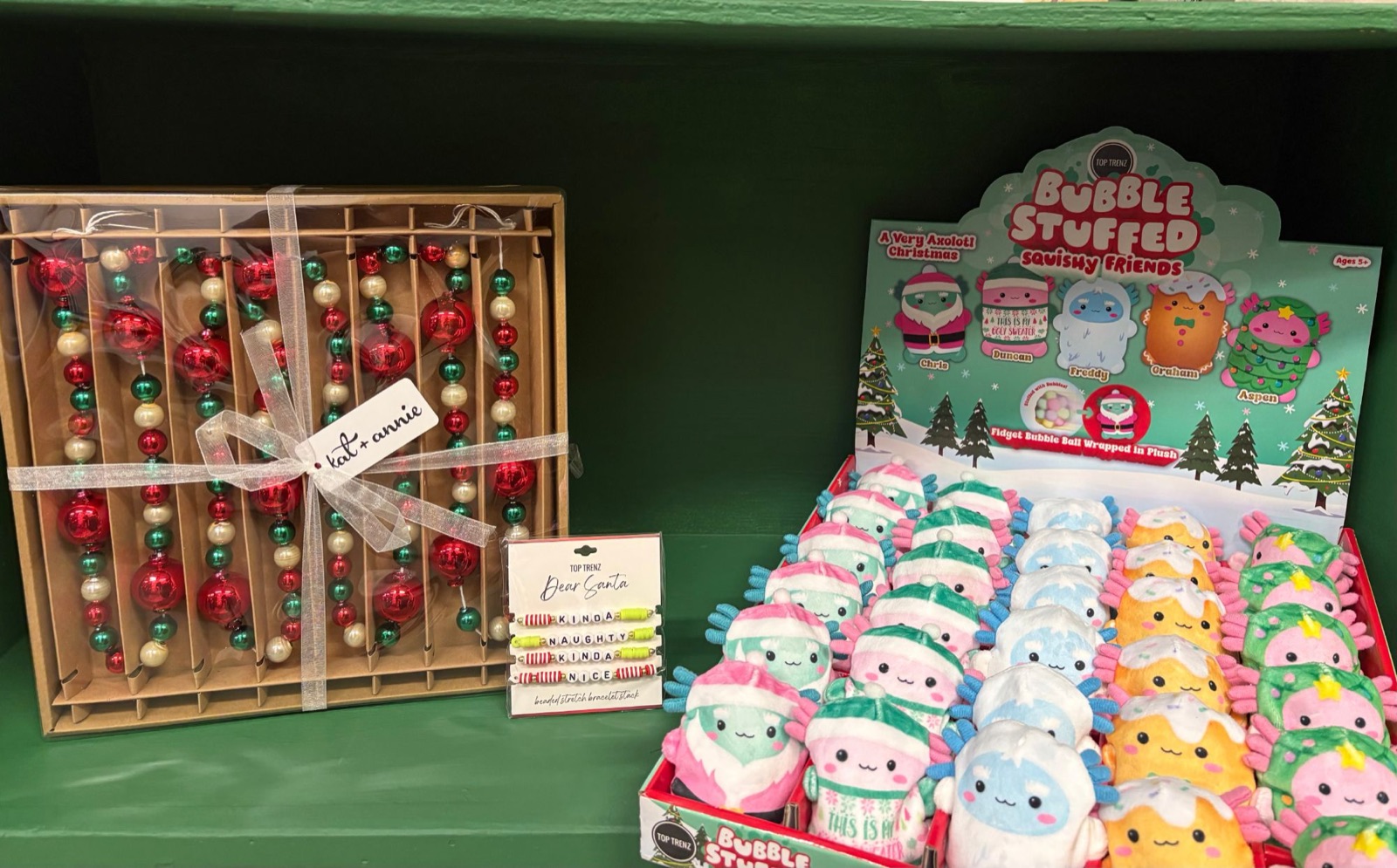 Boxed beaded garland, a bracelet set and plush squishy toys on a green shelf